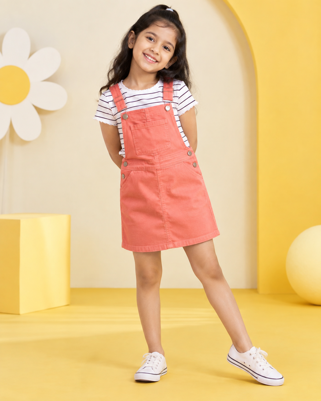 Girl wearing a coral dungaree dress with striped T-shirt